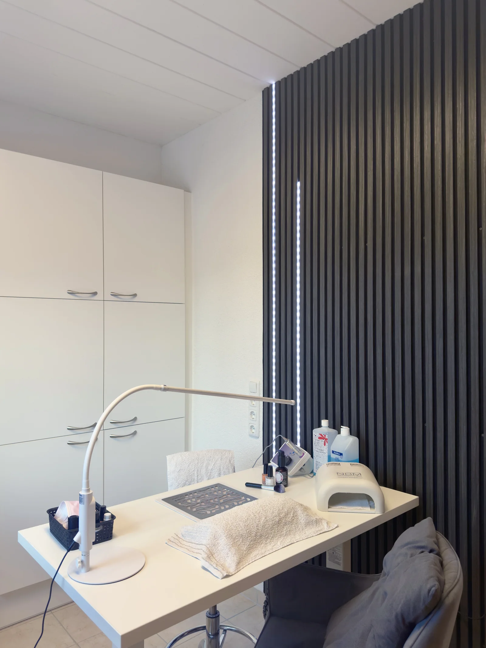 Maniküretisch mit Arbeitsleuchte und UV-Lichthärtungsgerät vor der Lamellenwand